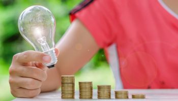 Hand holding light bulb with Coins stack on wooden table in the morning. Energy and Money saving , accounting and financial concept